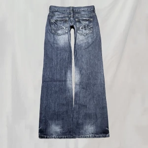 Lågmidjade jeans - Midja: 80 innerben:85 Lågmidjade jeans med vida ben och detaljerade bakfickor. Hittar ingen storlek men uppskattar passa kring en 36. Håller upp på bild då de va stora på mig. Nötningar vid ex fickor. Lite nötta fotändar men överlag mycket bra skick🤍