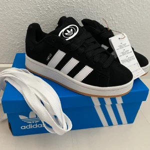 Nya svarta Adidas Originals Campus 00s j stl 36 (rymliga) - Oanvända och ligger kvar i kartong.  Innersulan är 23,5 cm Färg: Core Black/Cloud White/Cloud White.  Ingår svarta originalsnören från Adidas som sitter på. Jag skickar även med vita chunky skosnören som inte är av märket Adidas. Därav lägre pris!