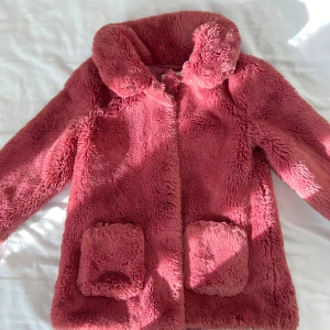 Barn jacka vinröd/lila färg  - Fin vinter jacka för ett barn. Fluffig & skön. Stängs framme med knappar & har två fickor på framsidan. Använts bara under en vinter säsong & efter har barnet växt ur den. Den är fortfarande i bra skick då vi bara använt jackan vid fina tillfällen. 