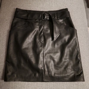 Kjol i skinnimitation  - Otroligt fin kjol i skinnimitation från H&M. Svart med fickor fram och skärp. Minilängd och högmidjad. Aldrig använd 