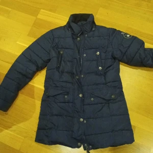 Längre ridjacka - Säljer längre ridjacka från märket Active. Fint skick förutom ett litet hål där man knäpper där bak. Går lätt att laga för den händige. Ska leta efter kapuschongen. 