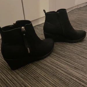 Skor med kilklack  - Svarta kilklackar i storlek 41. Använda ett fåtal gånger. Dekorativa dragkedjor på utsidan av skorna. 