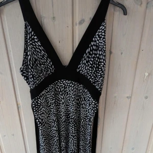 Vintage Svart och vit klänning med mönster,S/M - En elegant svart och vit klänning med ett unikt mönster som påminner om små löv. Klänningen har breda axelband och en knytning i midjan för en smickrande passform. Den är ärmlös och har en v-ringad halsringning.i mycket bra skick finns väldigt liten