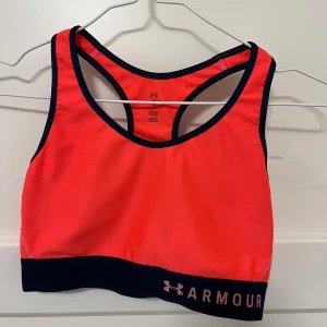 Under Armour sport-bh - Sportbehå från Under Armour. Storlek M. Neonorange/rosa med mörkblå linjer runt om. I mycket fint skick! 