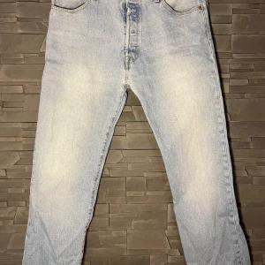 Ljusblå jeansbyxor - Ett par ljusblå 501 från Levis. Byxorna har en klassisk femficksdesign och är tillverkade i denim. De har en knappgylf och är i en rak passform. Sparsamt använda och är i mycket bra skick! Nypris 1099kr
