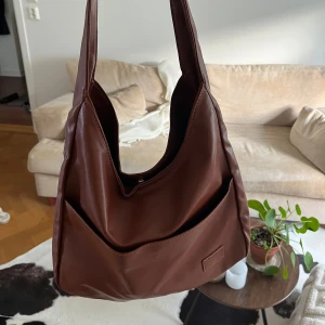 Brun väska i vegansk läder - Väskan är i nyskick och oanvänd. Mått: 30x25 och ca 50cm lång när man hänger den på axeln. Skriv för frågor💃