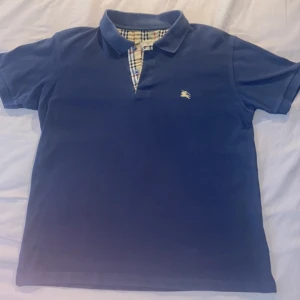 Blå Burberry Piké  - Säljer denna mörkblå pikén från Burberry Nypris 4100kr Lätt blekt på kragen  Modellängd 180 CM