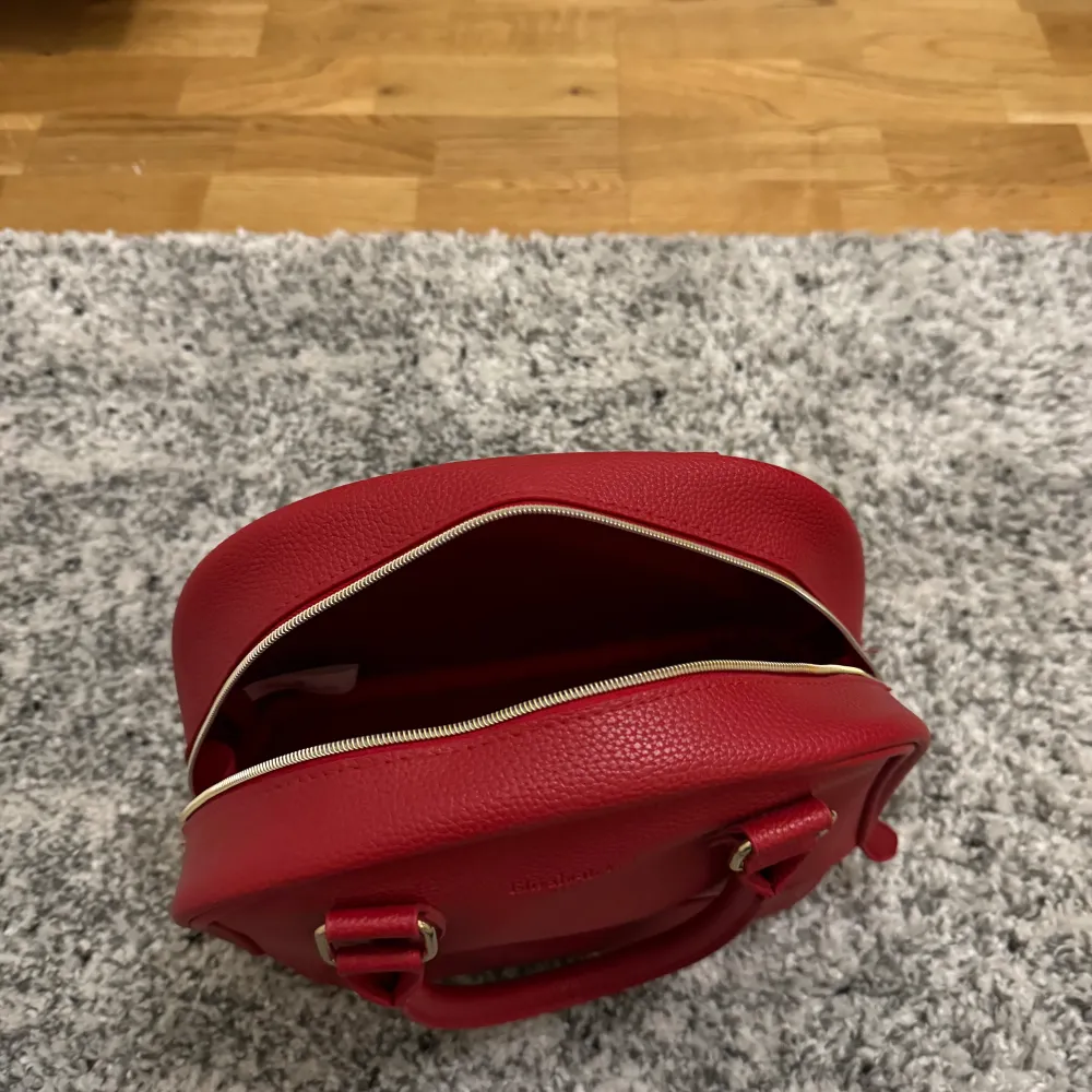 Hej! Säljer min fina röda hans väska med 2 fack. Ett övre och ett under, vilket gör att massa får plats.  Märke: Elizabeth Arden . Väskor.