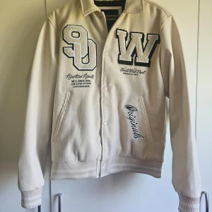 Jack & Jones beige jacka, storlek M - Jacka med en klassisk college-stil. Mjuk och bekväm passform, perfekt för att hålla dig varm under kallare dagar. Jackan har en snygg design med broderade detaljer och logotyp på bröstet. Den har också en ficka på insidan.  Oanvänd, endast testad!