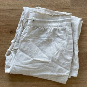 Ljusa linnebyxor - Ljusa (beige?) linnebyxor med fickor. Resår och knytning i midjan.   Obs! Ett svagt gult märke fram, men det syns ej när de är knutna