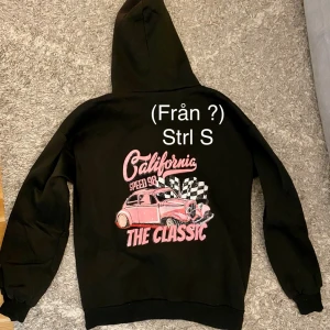 Hoodie - Hoodien har tryck på baksidan och är helsvart på framsidan med snören. Knappt använd.