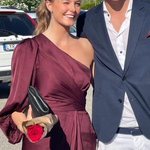 Leontine Dress By Malina - Leontine Dress är en One shoulder klänning av By Malina i färgen Deep Wine. Perfekt som balklänning eller andra tillställningar. Kan knytas i midjan på flera sätt, skriv för fler bilder. Endast använd två gånger.  Original pris: 2499 