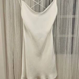 Vit satinklänning - Vit satinklänning från zara. Storlek XS. Använd men i fint skick. Klänningen har en ”utdragen” tråd framtill (bild 3), samt nedkortade band (bild 2). 