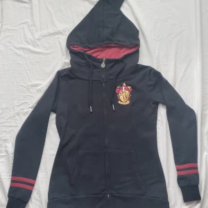 Harry Potter hoodie - Harry Potter merchandise hoodie köpt på EMP. Har en väldigt stor och trevlig luva som är spetsig, och en hög krage. Den är rätt så slim fit och ganska lång. Endast använd ett fåtal gånger, nypris 750 kr. 