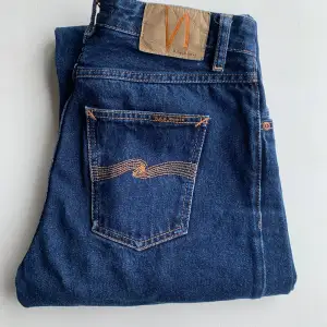 Perfekta raka mörkblå jeans från Nudie Jeans. Jeansen är i bra skick, endast använda ett fåtal gånger. Jeansen är i storlek midja 28 och längd 32cm. Har en liten skada på vänster bakficka. Ursprungligt pris: 1400 SEK Obs: köparen står för frakten!