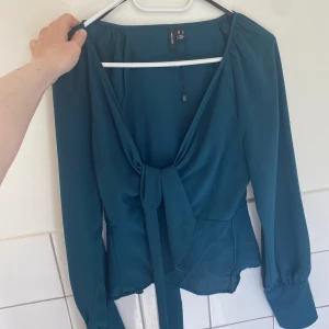Snygg mörkgrön blus  från vero Moda  - Använd  en gång  Man kan ha den på lite olika sett så det är ett snöre som går runt bakom bakom  & sen knyter man den  Mörkgrön men den ser blå ut på bilden  Lite urringad 