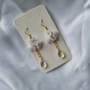 Waterdrop Lily Dangle Earrings - Dessa eleganta örhängen passar perfekt för att upphöja dina outfits eller som en gåva till en vän. Ploppar ingår.  Material: Guldfärgad metall,  blomsterpärlor, vattendrops-pärlor, bakstycken  Alla beställningar från oss kommer fint paketerade 🤍