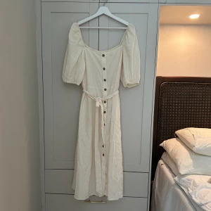 Vit somrig klänning - Väldigt fin somrig klänning med knytning i midjan och knappar hela vägen. Puffärmar. Midiklänning. I bra skick. 