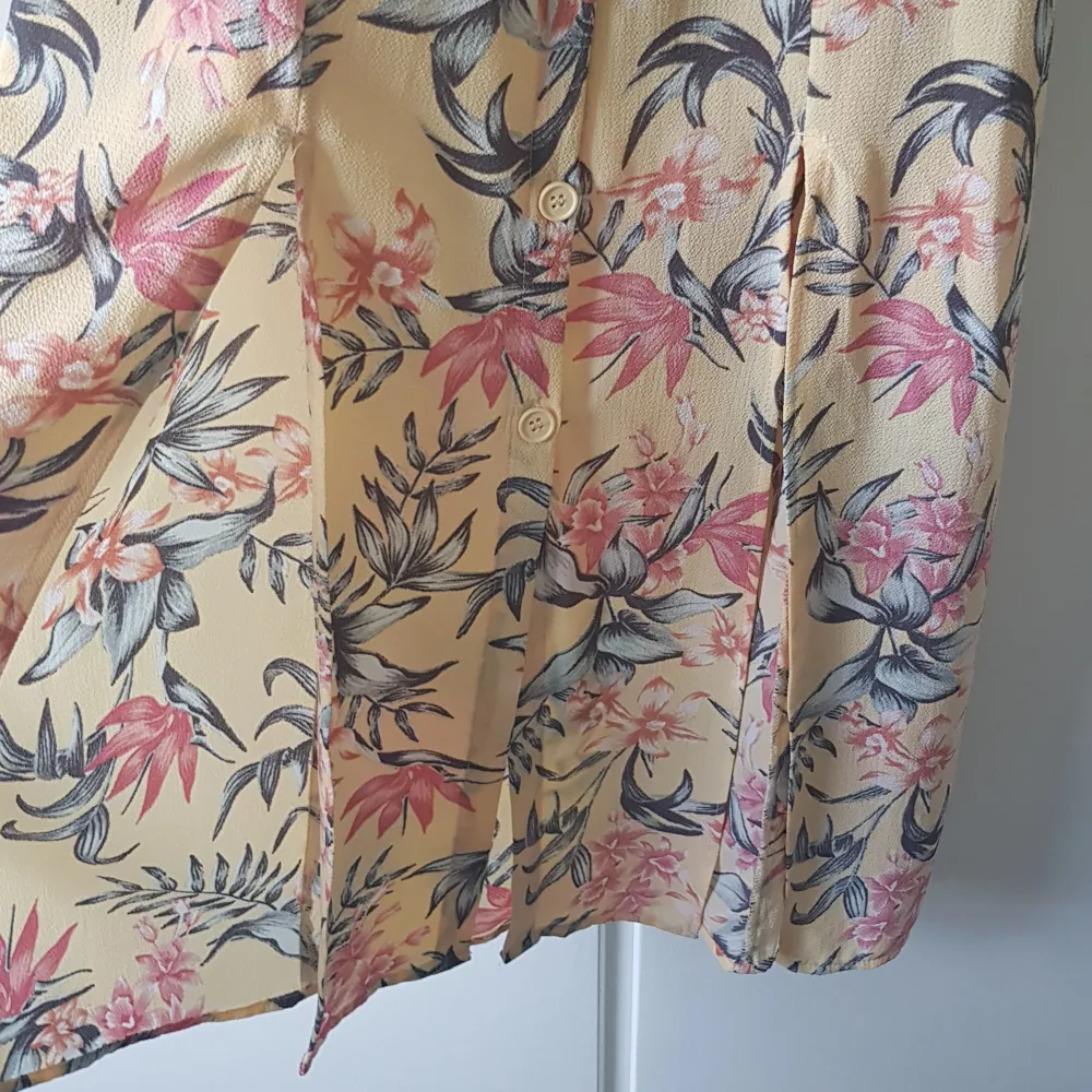 En pastell gul och lång sundress med blommigt motiv i korall färg och svartvitt. Framsidan har knappar hela vägen ner och sen två slit på var en sida för att visa lite extra ben.. Klänningar.