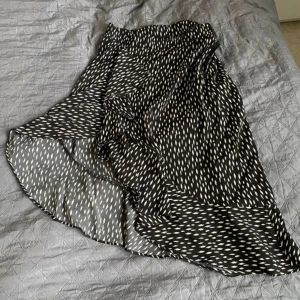 Svart och vit mönstrad kjol - En svart volang-kjol med vita mönster. Kjolen har en omlott-design och volangdetaljer. Den är tillverkad i ett lätt och flödande material.💕