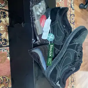 Ett par svarta sneakers från Nike med svarta sömmar. Skorna har en autenticitetsmärkning från StockX och kommer med extra röda skosnören och svartvit. Både box och ytrebox kommer med och två svartvita bandanas. 