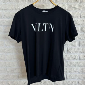 Svart t-shirt från Valentino - En svart t-shirt från Valentino med vit text 'VLTN' tryckt på framsidan. T-shirten har korta ärmar och en rund halsringning.