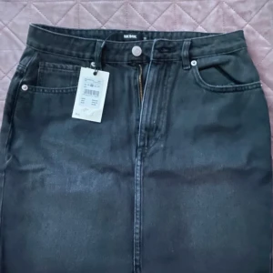 Svart jeanskjol från Bik Bok - En svart jeanskjol från Bik Bok med dragkedja och knapp framtill. Kjolen har fickor både fram och bak.