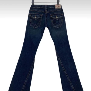 Mörkblå True religon jeans - Mörkblå jeansbyxor med dekorativa bakfickor och knappar. Byxorna har en klassisk design med en utsvängd passform. True religions jeans!
