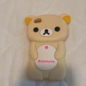 Rilakkuma mobilskal - Ett sött mobilskal i form av Rilakkuma, en beige björn med gula öron och en vit mage. Skalet har en öppning för kameran och är designat för att passa en specifik mobilmodell.