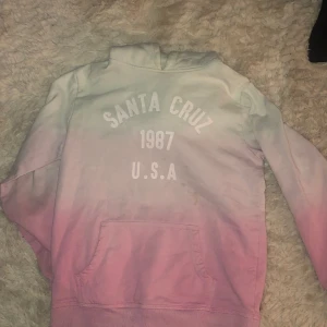 En rosa/blå hoodie - En rosa blå tröja med vit text där de står grejer läs på bilderna en luva och ficka  Det är nån liten brun fläck på den men de går nog bort i framtiden 