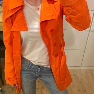Orange trenchcoat  - Trenchcoat i ascool färg! Den riktigt lyser. Ser inte använd ut. Köpt för 1000 kr men säljer för 500