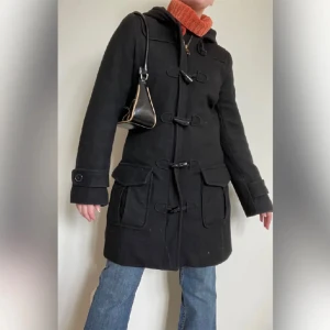 Ullkappa med luva  - Kappa i ull och med luva från H&M. Köpt på Plick men ej kommit till användning. Tjock och varm. Stängs med dragkedja och duffleknappar. Fint skick! Bilderna är lånade!! 