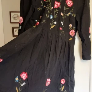 Sommarklänning blommig klänningė - Svart klänning med härlig vidd i kjolen. En riktig snurrkjol Härlig brodyr med rosor. Blommor Lite vintage bohemstil midsommar Säljes pga fel storlek. Blev ej använd