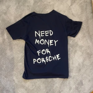 Marinblå t-shirt - En riktigt fet t-shirt som är perfekt nu på sommaren. Hög kvalite på materialet. Tröjan har ett tryck på ryggen där det står ”need money for porsche”. Storleken är S. Har en likadan fast i vit färg på min profil. Skriv vid funderingar. 👕