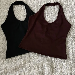 Svart och brun halterneck toppar - Två halterneck toppar i storlek S, en i svart och en i brun färg. Topparna har en enkel design med djup urringning och är ärmlösa. Materialet påminner om baddräktsmaterial.  Båda 2 för 40kr. 