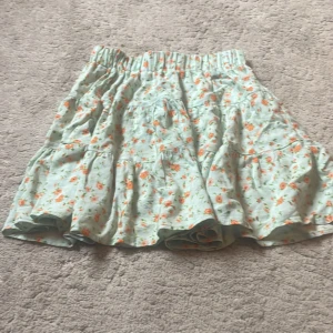 Bershka kjol  -  en få använd kjol i storlek xs. Kommer ej till användning på grund av för många kjolar. Jättefin till sommaren. turkos med orangea och lite gröna blommor. Kort kjol.