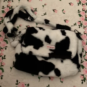 Axelremsväska med koskinnsmönster - En supermjuk stor axelväska med svartvitt koskinnsmönster💓Väskan har en justerbar axelrem och en dragkedja för säker förslutning. Insidan är fodrad med ett ljust tyg och har en innerficka med dragkedja!🫶🏻