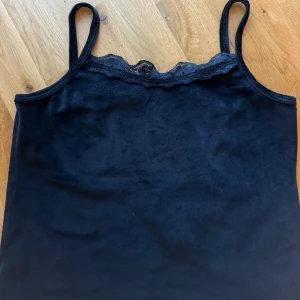 Svart linne med spetsdetaljer - Säljer ett snyggt svart linne med spetsdetaljer vid halsringningen. Linnet har smala axelband och är tillverkat i ett mjukt och bekvämt material. Perfekt för både vardag och fest! ny 