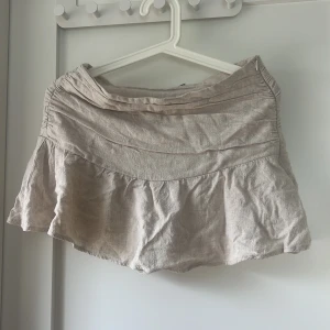 Beige kjol från Stradivarius - En beige linne material kortkjol/ miniskirt från Stradivarius. Det är en skort så det är små mini shorts under vilket är super. Kjolen har en volangdetalj och är tillverkad i ett lätt och luftigt material. Säljer för att den inte passar mig längre vilket är synd men hoppas någon annan kan ha nytta av den!! :) 