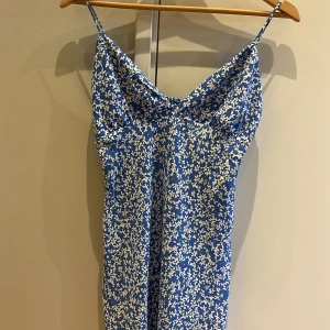 Blå blommig klänning - Säljer en superfin blå klänning med vita blommor. Den är ärmlös och har smala axelband. Klänningen är i ett mjukt och skönt material, perfekt för sommaren. Den har en tight passform i midjan och är en kortklänning. Perfekt för fest eller en dag i Grekland!🇬🇷 