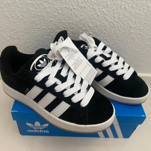 Nya Adidas Campus 00s -storlek 38 - Adidas Originals Campus 00 s j Storlek: 38 Färg: Svarta (Core Black / Cloud White / Cloud White) Ingår både vita och svarta skosnören.  Nya och oanvända. Ligger kvar i kartong. 