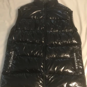 Väldigt fin Moncler väst med QR kod - Säljer en snygg Moncler väst i väldigt fint skick vad  jag kan se. Kan inte hitta något som skulle kunna vara fel med den. Den har en QR kod och är väldigt skön att ha på sig. Passar i de flesta väder. Storleken är XL  men passar Large och Medium. 