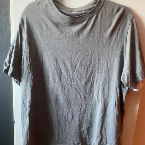 Grå t-shirt - Grå t-shirt köptes secondhand, säljer då jag inte får användning för den. Har används ett fåtal gånger, har inga tecken på användning. Normal till storlek. Finns på flera sidor. Köparen står för frakten.