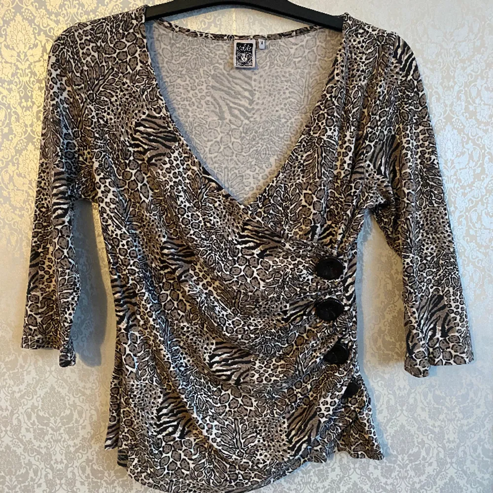 It has a early 00s vibe and is in good condition, it’s a size M, but very stretchy, would fit M-XL. It has different type of safari animal print, it has decorative buttons on the side.. Toppar.
