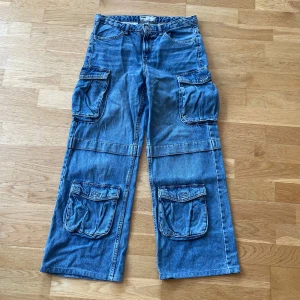 Blå cargobyxor från Bershka - Säljer ett par blå cargobyxor från Bershka i denim. Byxorna har flera praktiska fickor och en avslappnad passform. Perfekta för en casual look. 🦋