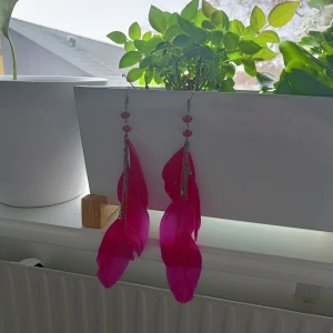 Rosa fjäderörhängen med kedjedetaljer - Snygga och iögonfallande rosa fjäderörhängen med silverfärgade kedjor och rosa pärlor. Perfekta för att ge en färgklick till din outfit. Strass