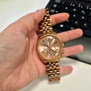Klocka från Michael Kors (MK5569) - Säljer en elegant, klassisk guldfärgad (med hint av roséguldfärg) klocka från Michael Kors i rostfritt stål. Klockan är vattentålig, drivs av kvartsbatteri, har datumvisning och tidtagning (kronograf) och är i mycket fint skick. Boetten har 38 mm i diameter.