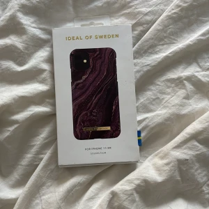 Lila mobilskal från iDeal of Sweden - Säljer ett snyggt mobilskal till iPhone 11/XR från iDeal of Sweden. Skalets design har ett marmorerat mönster i lila och svart med inslag av guld och en liten guldfärgad detalj med varumärket på baksidan.