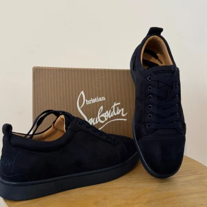 Christian Louboutin Mörkblå Mockasneakers – Lyx & Stil - Dessa exklusiva sneakers från Christian Louboutin är sinnebilden av modern elegans. Tillverkade i lyxigt mörkblå mocka kombinerar de tidlös design med sofistikerad attityd. Den rena silhuetten och de ton-i-ton-färgade detaljerna skapar ett diskret men distinkt intryck – perfekt för dig som vill sticka ut med stil.  Med Louboutins ikoniska röda sula som subtilt signum får varje steg en touch av haute couture. Oavsett om du bär dem till en avslappnad kostym eller jeans med skjorta, lyfter dessa sn