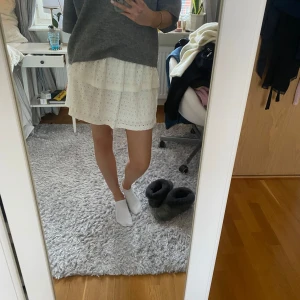 Vit kjol med spetsdetaljer - Söt vit kjol med spetsdetaljer och volanger. Perfekt för en somrig look. Den har en elastisk midja för bekväm passform.